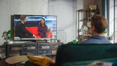Jeune homme beau assis dans une pose détendue sur un canapé et regarder la télévision avec talk-show en direct pendant la journée le week-end. Sérieuse Africaine