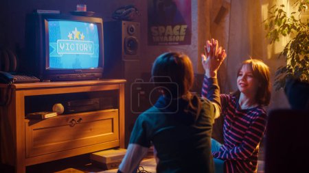 Concept d'enfance nostalgique : Jeune garçon et fille jouant à un jeu vidéo d'arcade de la vieille école sur un téléviseur rétro installé à la maison dans une pièce à l'intérieur correct pour la période