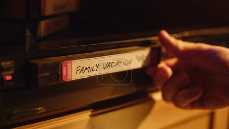 Gros plan d'une personne insérant une cassette VHS dans un lecteur avec des images de vacances heureuses et nostalgiques de la caméra vidéo domestique. Technologie rétro des années 90