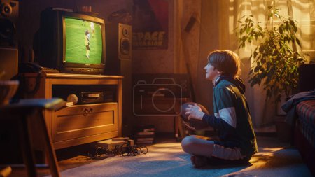 Jeune fan de sport Montres match de football américain sur Retro TV dans sa chambre avec intérieur daté. Garçon soutenant son équipe préférée, se sentant fier quand