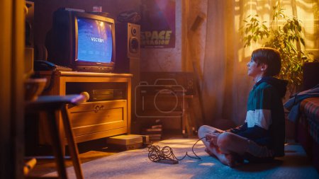 Beau enfant jouant 2D Arcade Space Shooter jeu vidéo sur une console à la maison dans sa chambre avec l'intérieur des années 80. Jeune garçon atteint la fin du niveau et