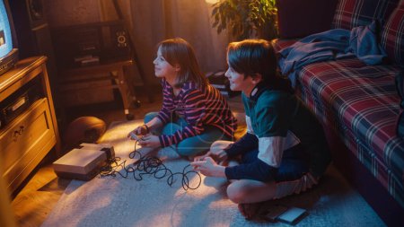 Nostalgic Childhood Concept : Young Brother and Sister jouant au jeu vidéo d'arcade vintage 8 bits en 2D sur un téléviseur rétro installé à la maison dans une pièce avec période