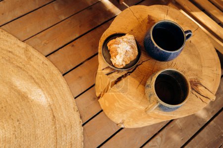 Téléchargez les photos : Petit déjeuner matinal en plein air, thé et croissant sur une table en bois. Nourriture pour camping, plats à emporter, restauration. Table en forme de bûche - en image libre de droit