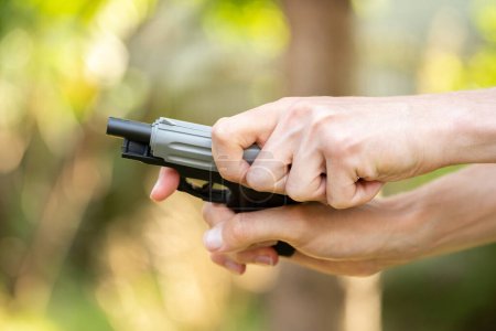 Photo for Anonymous man cocking a toy gun, reloading a small handgun, hands closeup, detail, shallow dof, outdoors shot. Gun laws, policies and early education abstract concept. Weapons and law regulations - Royalty Free Image