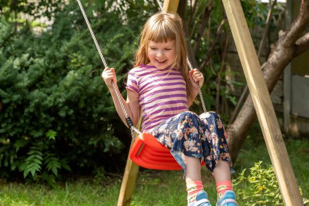 Photo for Happy girl, elementary school age child sitting swinging on an simple outdoor swing in the backyard, copy space, one person. Leisure activities, recreation concept, having fun outdoors, playground - Royalty Free Image
