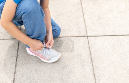 Photo for Young anonymous girl, elementary school age child tying her shoe, shoelaces. Child tying shoes outdoors hands closeup, detail, copy space. Generic modern kids footwear simple concept, one person - Royalty Free Image