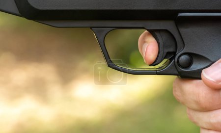 Photo for Man pulling the trigger of an air gun airgun, firing a pneumatic weapon, finger on the trigger side view, object detail, extreme closeup, one person shooting a pistol, about to shoot. Gun laws concept - Royalty Free Image