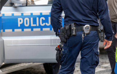 Polish police vehicle and a policeman equipment, gun, handcuffs utility belt detail, closeup. Polish policemen, emergency response services, safety, security concept