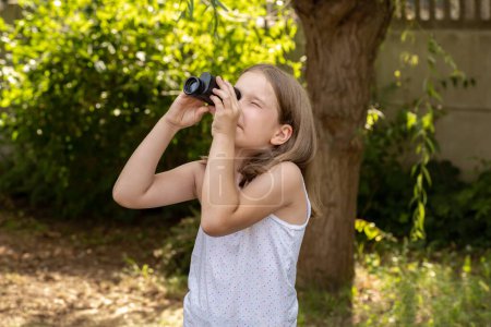 Téléchargez les photos : Jeune enfant d'âge scolaire, fille regardant dans le ciel à travers une loupe monoculaire observant les oiseaux, cherchant quelque chose dans le ciel. Opportunités et possibilités concept abstrait - en image libre de droit