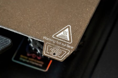 A 3D printer heated bed building pad hot surface warning label seen from up close, nobody. 3D printing equipment and accessories simple concept, device usage instructions warning icons symbols detail
