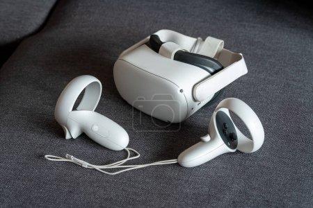 Téléchargez les photos : Casque de réalité virtuelle Meta Quest 2 avec contrôleurs sur un canapé. Jeux et expériences VR autonomes sans fil et filaires, technologie Metaverse, concept simple de jeu VR - en image libre de droit