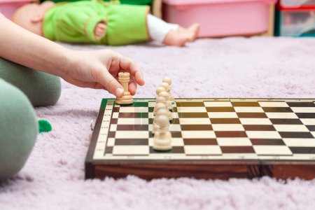 Childs hand ergreift einen Bauern auf einem Schachbrett, das für eine Partie aufgestellt ist, junges intelligentes Mädchen, aufgewecktes cleveres Kind, das Schach lernt, entspanntes und pädagogisches Umfeld zu Hause abstraktes Konzept, Nahaufnahme, Kopierraum