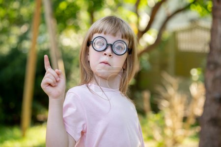 Girl, child with big large funny glasses pointing her finger upwards, eureka gesture, coming up with an idea. Smart intelligent kid abstract concept, symbol, one person. Children education, learning