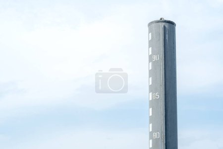 Water level gauge indicating the waters depth at a harbor against a backdrop of a light blue cloudy sky, copy space background. Measuring depth of a body of water simple concept, nobody, no people