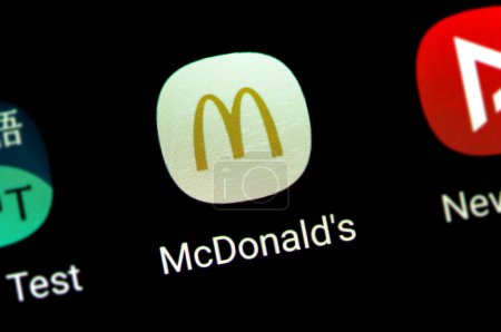 Foto de Una vista ampliada de la pantalla de un teléfono inteligente que muestra el icono de la aplicación McDonalds rodeado de otros iconos de la aplicación, entrega rápida del pie, aplicación de la marca McD en un teléfono inteligente - Imagen libre de derechos