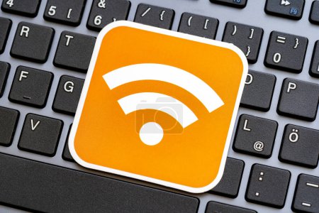 A vibrant orange label badge displaying the universal general Wi-Fi signal strength symbol atop a black desktop PC computer keyboard, wireless network connectivity and internet access abstract concept