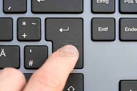 Finger captured in the moment of pressing the Enter key on a sleek modern design keyboard, submission of data, sending a message, chatting, adding to cart simple abstract concept, one person, top view