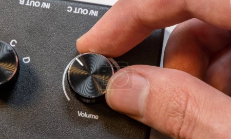 Anonymous man fingers finely tuning a volume knob on a sleek audio device control panel, adjustment of sound levels, gain control, turning music up, or turning down, sound controls abstract concept