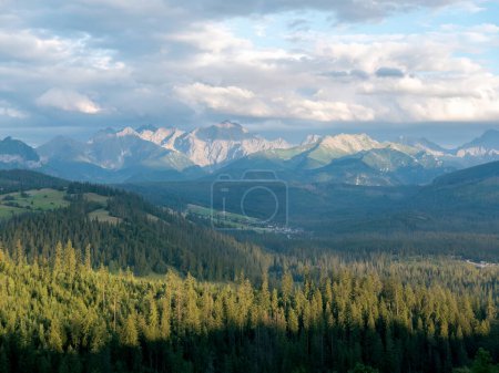 Stunning landscape of the Tatra Mountains with a lush, green forest in the foreground under a beautiful cloudy sky, afternoon, Polish Tatra mountain range calm serene shot, Europe travel destinations