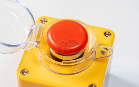 Nahaufnahme eines roten Not-Aus-Knopfes mit einem schützenden transparenten Gehäuse auf einem gelben Panel, Sicherheitsmechanismus für die Stilllegung schwerer Industrieanlagen, Arbeitsschutzbestimmungen, Richtlinienkonzept