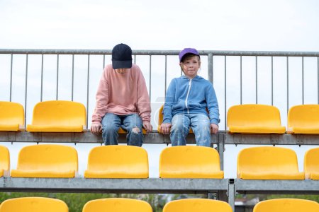 Two young girls, children sitting on stadium seats, bleachers, chairs, empty space, happy cheerful kids on a sports event audience, sport and recreation, two people, lifestyle shot