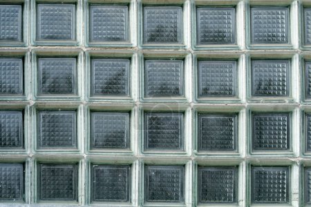 Close-up view of a symmetrical and textured glass block wall, old 80s 90s building design, thick square glass pattern, nobody, front view, high resolution material background texture, frontal shot