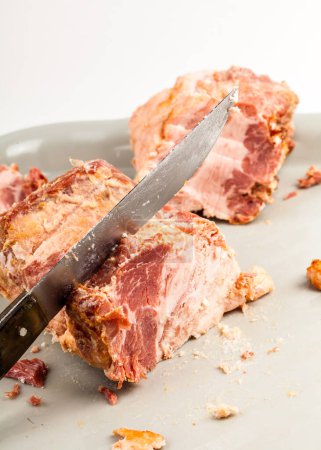 Carving a piece of tender pork roast with a sharp knife on a light background, exposing the succulent meat, object closeup, nobody, vertical shot wallpaper backdrop, no people. Meat products concept