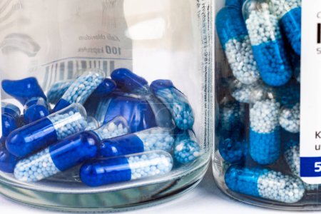 Capsules blanches bleues avec des granules à l'intérieur dans des bocaux en verre transparent, présentant des produits pharmaceutiques, des médicaments, des médicaments comprimés génériques comprimés gros plan détail, personne. Concept d'achat de médicaments
