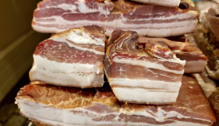 Stacked thick cuts of bacon with visible marbling of fat and meat on display, showcasing the products freshness and high quality, group of objects detail, nobody. Prepared smoked meat products concept