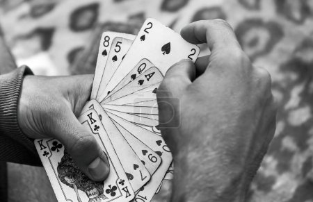 Black and white dramatic close-up of hands holding a variety of playing cards spread, poker, gambling addiction simple abstract concept symbol, one anonymous person, social issues, closeup detail