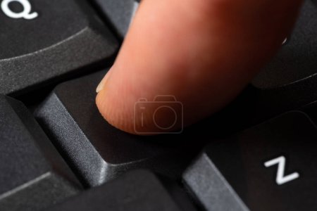 Nahaufnahme eines Fingers mitten im Geschehen, während er eine nicht beschriftete schwarze Taste auf einer modernen Computertastatur drückt. Handeln, jeder Tastendruck, anonyme Benutzereingabe einfaches abstraktes Konzept, eine Person