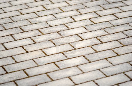 Detailed view of the pattern and texture of worn grey paving bricks laid out outdoors, simple minimal backdrop background texture, angle shot, no people. Rectangle paving bricks outside, shallow DOF
