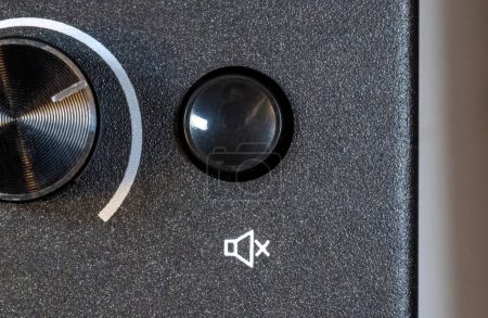 Close-up view of a simple mute button with a generic mute symbol on a simple audio device appliance, top view, from above, detail closeup. Muting sound turning audio output off abstract concept, quiet