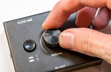 Close-up view of a mans hand turning up adjusting the volume knob on a modern audio device. Making audio output quieter or louder simple concept, one person, detail shot. Audio appliances usage