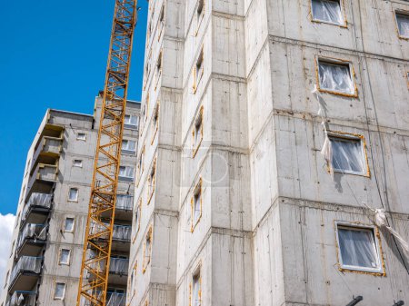 Multi-story residential block under construction, with exposed concrete walls and a yellow crane beside it. Housing development industry, new real estate, business market abstract concept, news shot