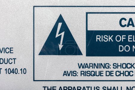 Una vista de cerca de una etiqueta de advertencia bilingüe que detalla el riesgo de choque eléctrico desde un dispositivo o dispositivo de la máquina, con un gran símbolo de rayo dentro de un triángulo, macro detalle, nadie