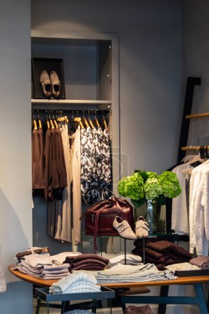 Téléchargez les photos : Intérieur d'une boutique de vêtements élégante avec des présentoirs de vêtements et de chaussures sur une table et suspendus aux rails - en image libre de droit