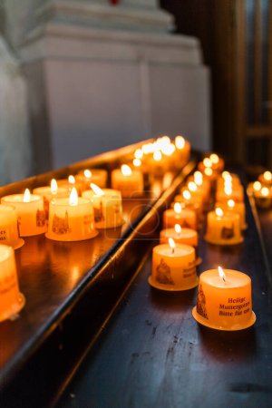 Téléchargez les photos : Grand groupe de bougies votives lumineuses courtes sur des étagères en bois utilisées pour les prières à l'intérieur de l'église sombre - en image libre de droit
