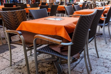 Téléchargez les photos : Tables de restaurant avec des nappes orange vif et des fauteuils confortables dans un café de rue ou un restaurant en plein air - en image libre de droit