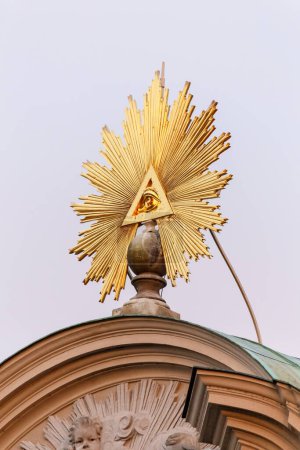 Téléchargez les photos : Œil de Providence sculpture dorée avec des poutres divergentes comme décoration sur le toit du bâtiment religieux, angle bas contre le ciel gris - en image libre de droit