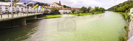 Téléchargez les photos : Panorama d'une large rivière verte coulant sous un pont alors qu'elle traverse une ville de la campagne verdoyante - en image libre de droit