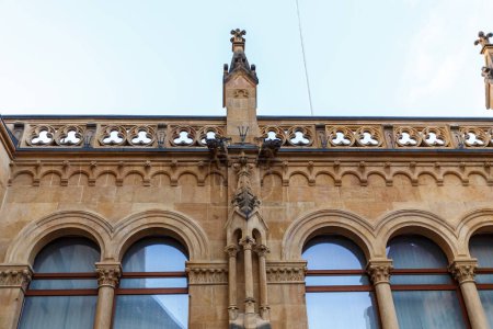 Téléchargez les photos : Ancien bâtiment historique en pierre avec trèfles le long du balcon ou du bord du toit et fenêtres voûtées regardant par en bas - en image libre de droit