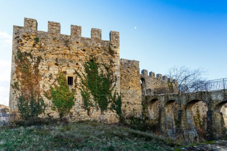 Foto de Antigua fortaleza de piedra almenada con enredaderas creciendo en las paredes y acceso a través de un puente arqueado visto de cerca ángulo bajo - Imagen libre de derechos