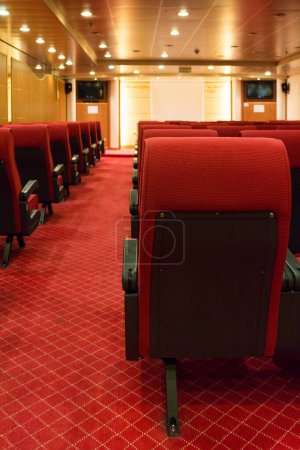 Foto de Interior de un pequeño cine o sala de visualización con lujosos asientos rojos y pasillo alfombrado visto desde la parte posterior mirando hacia la pantalla - Imagen libre de derechos