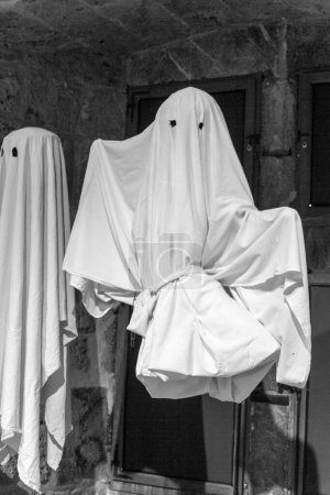 Téléchargez les photos : Costume d'Halloween effrayant d'un fantôme effrayant fabriqué à partir d'une feuille blanche ceinturée avec des trous d'oeil affichés sur un cadre dans une image à l'échelle grise - en image libre de droit