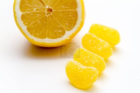 Téléchargez les photos : Citron frais coupé en deux avec des bonbons au citron sous la forme de segments jaunes affichés sur un fond blanc - en image libre de droit