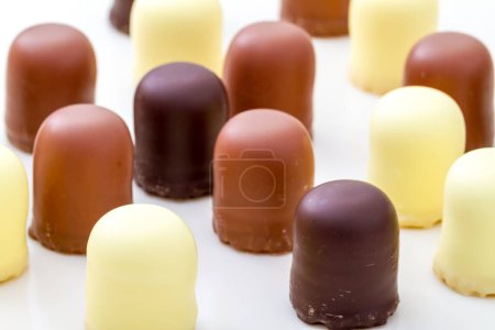 Téléchargez les photos : Bonbons au chocolat assortis en chocolat blanc, au lait et noir exposés sur une surface blanche en gros plan - en image libre de droit