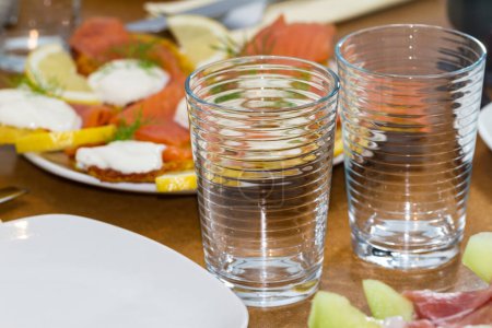 Téléchargez les photos : Deux grands verres vides propres sur une table à manger avec salade Caprese et assiettes vides dans un buffet ou un restaurant - en image libre de droit