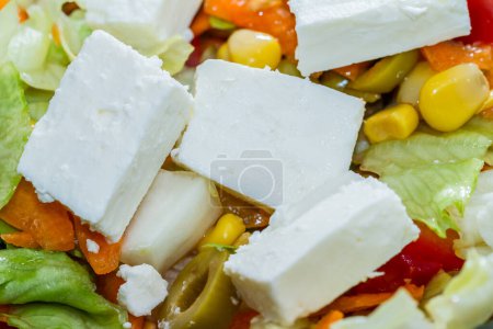 Téléchargez les photos : Cubes de fromage Feta grec semi-fondu à base de lait de chèvre ou de brebis dans une salade fraîche mélangée en gros plan vue arrière-plan complète - en image libre de droit