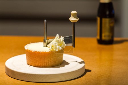 Téléchargez les photos : Roue de fromage mûr à raser avec une lame tranchante sur un couteau rotatif sur une table en bois à utiliser comme garniture et garniture - en image libre de droit